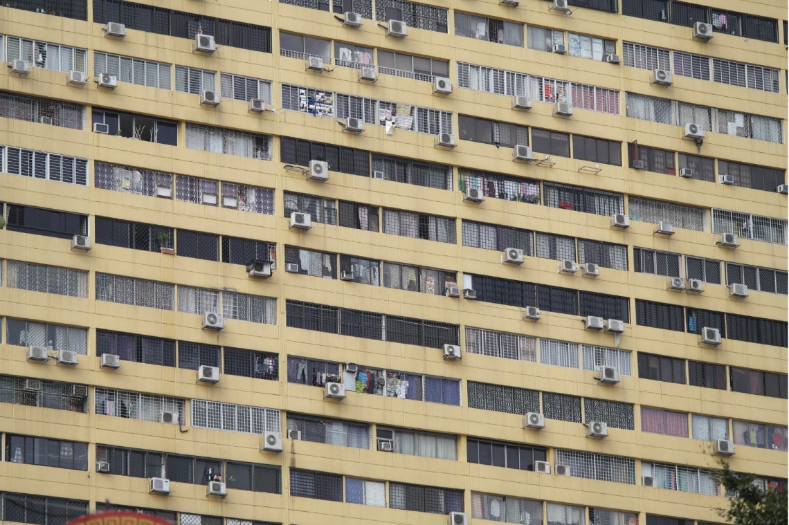 Exterior of a residential high-rise building in Singapore with dozens of AC units hanging from windows.