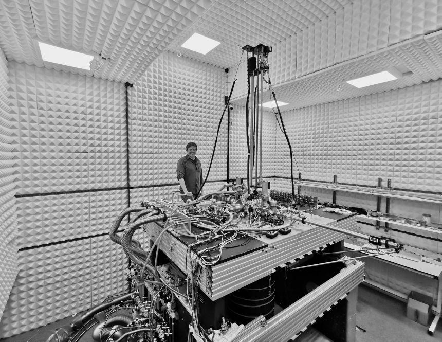 Researcher in an acoustically isolated lab with a complex array of cables, vacuum chambers, and control systems forming a scanning tunneling microscope used for quantum materials research.