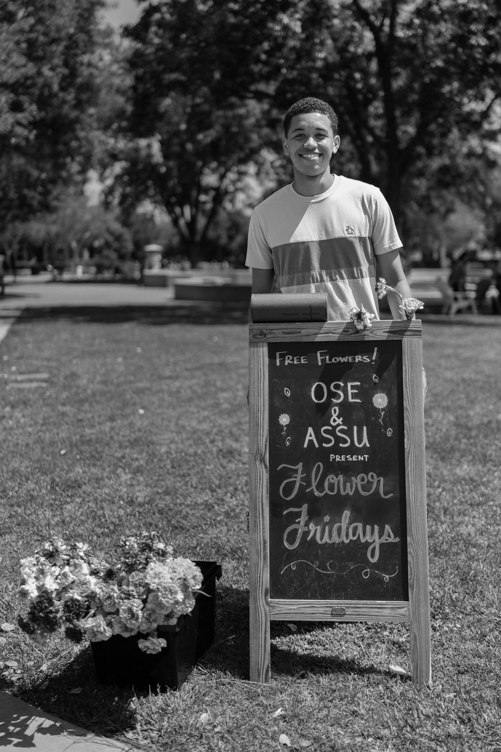 Image of Diego Kagurabadza posing for a photo with a sign that says Flower Fridays.
