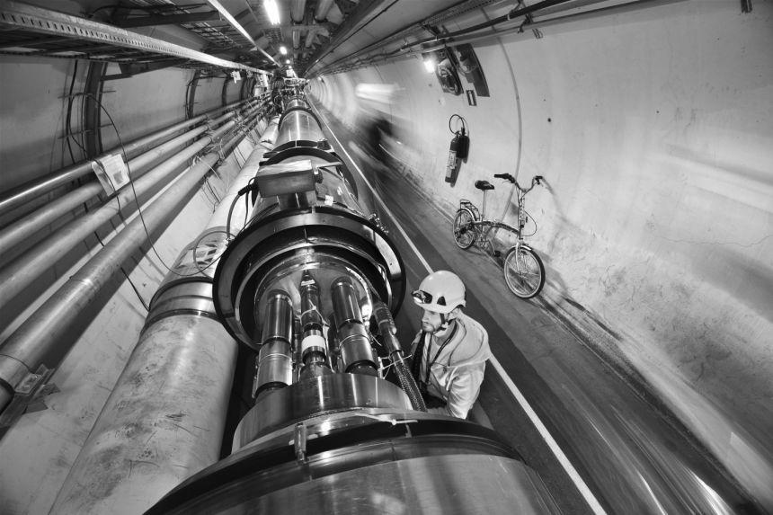 A man wearing a hard hat stands by a tubular section of the Large Hadron Collider at CERN, in an underground tunnel.