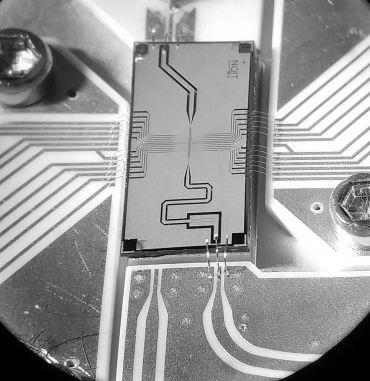 A rectangular quantum computing chip against a circuit board background.