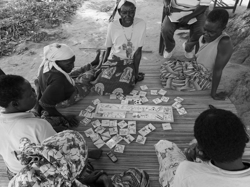 A mixed group of African participants sits on the ground around a board. On the board are small cards with different icons on, spread out.