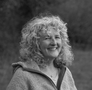 Dr Ruth Feber smiling outdoors, wearing a grey fleece jacket with trees and grass in the background