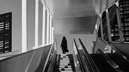 Early evening at modern business district with silhouette of businesswoman on top of a moving escalator.