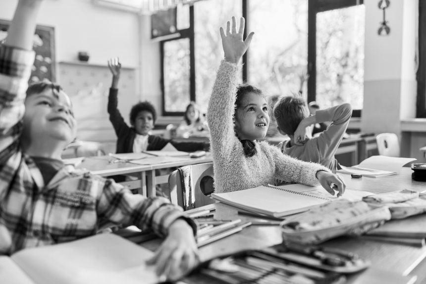 Children in classroom raising hands