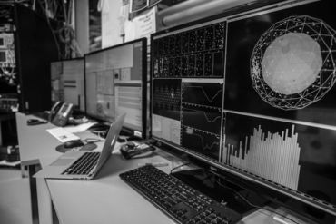 A bank of three computer screens showing graphs, data and simulations.