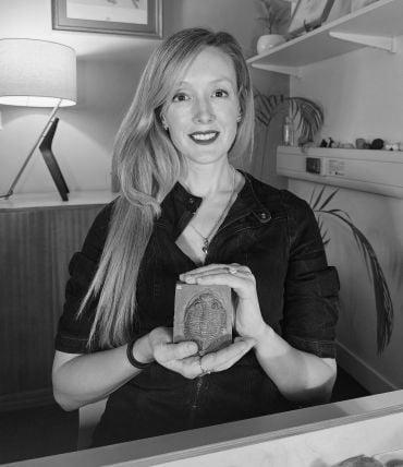 Professor Erin Saupe - a white lady with long blonde hair - holds a fossil trilobite in an office.