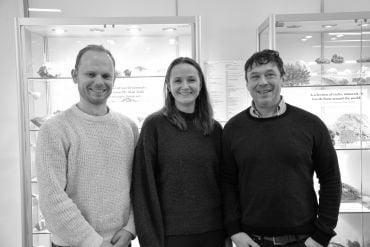 Dr Simon Stephenson (white man, brown hair), Associate Professor Claire Nichols (white lade, long brown hair), Associate Professor Jon Wade (white man, dark hair). They stand in front of two cabinets containing rocks and shells.