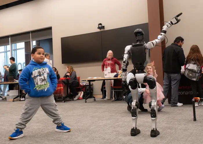 A boy stands next to a bipedal robot.