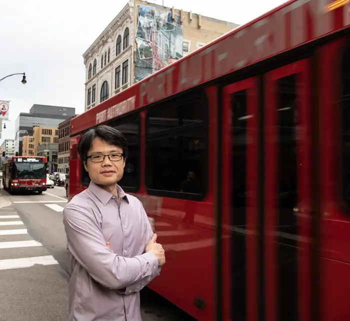 Sean Qian photographed as a bus passes behind him in Pittsburgh.