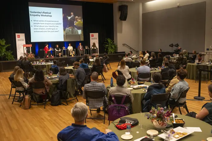 A group of people gather and sit around tables in a large room.