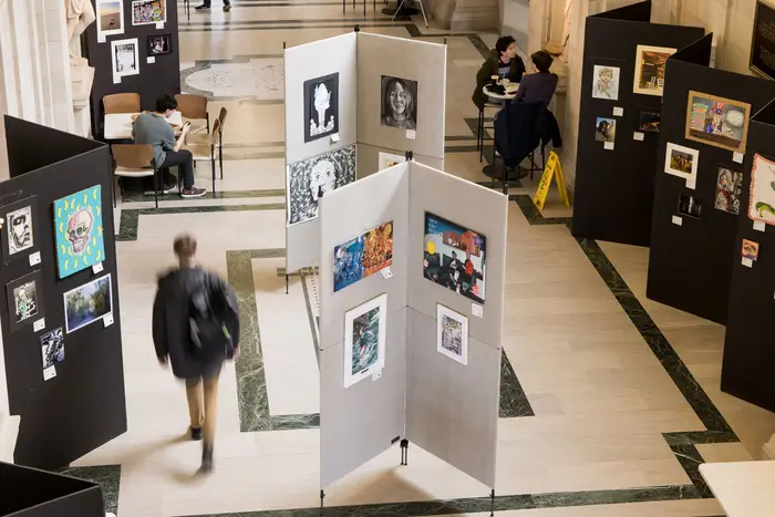 An out-of-focus student walks among displays exhibiting pieces of art.