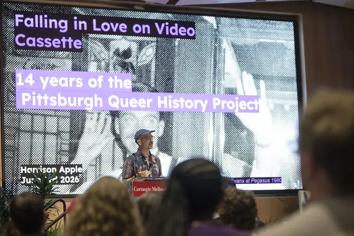 A person stands behind a podium in front of a screen that says